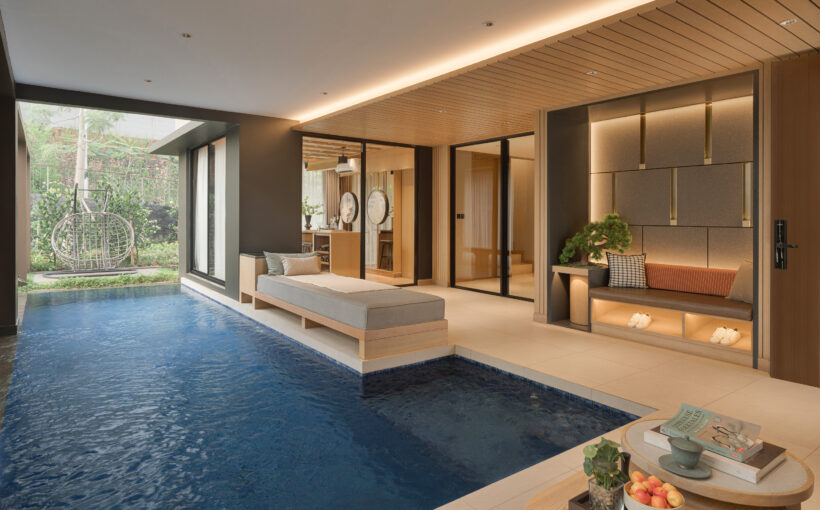 A serene living space featuring a large window overlooking a lush garden, with a modern wooden interior, a light-colored sofa, and an indoor pool area.